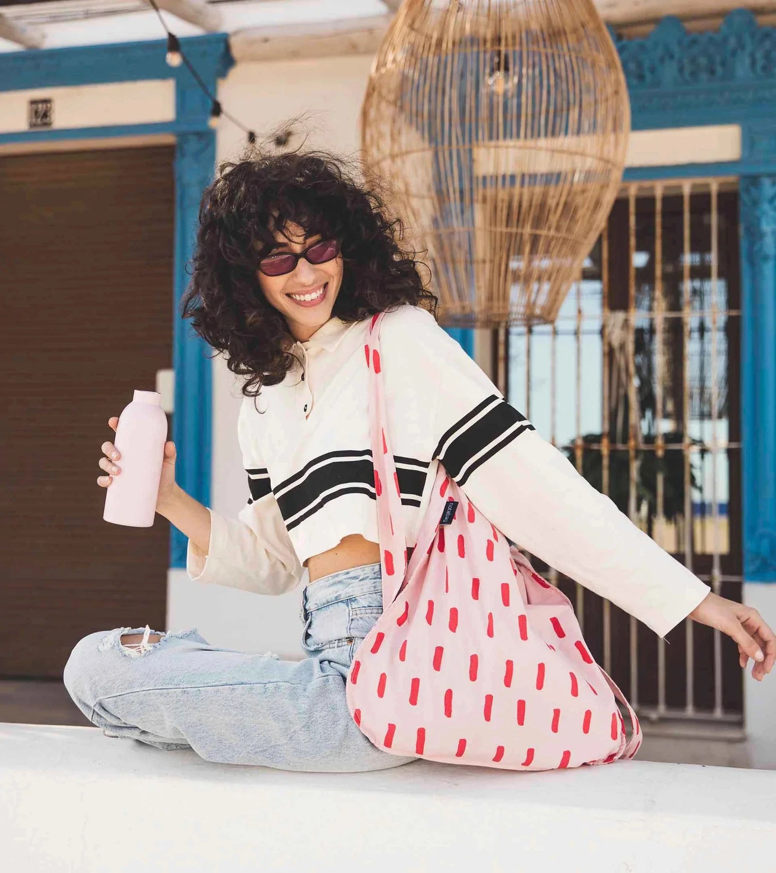 Woman sits on a ledge holding a water bottle and an eco-friendly reusable bag