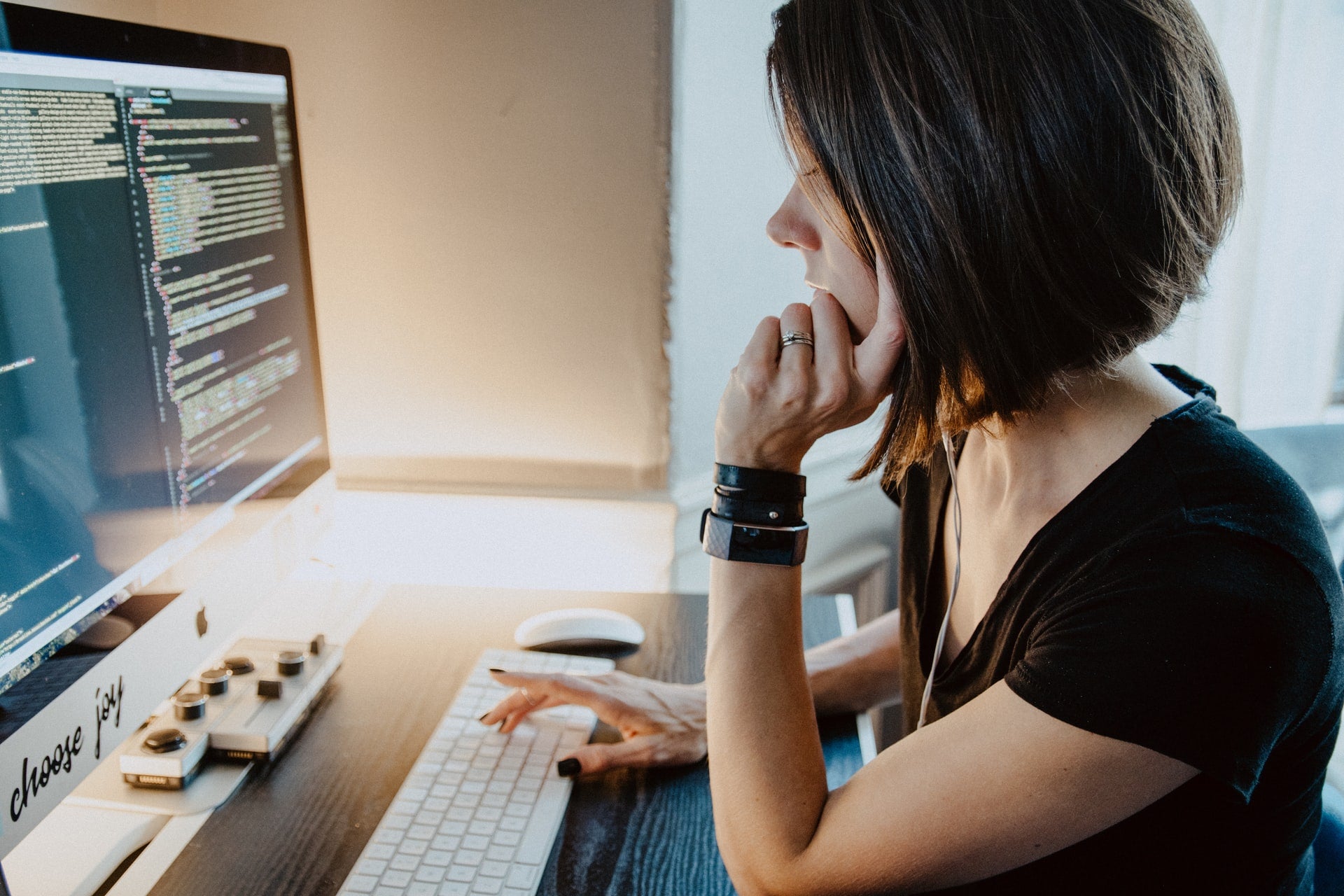 profile of woman sitting, chin in hand, at desktop computer, compiling code