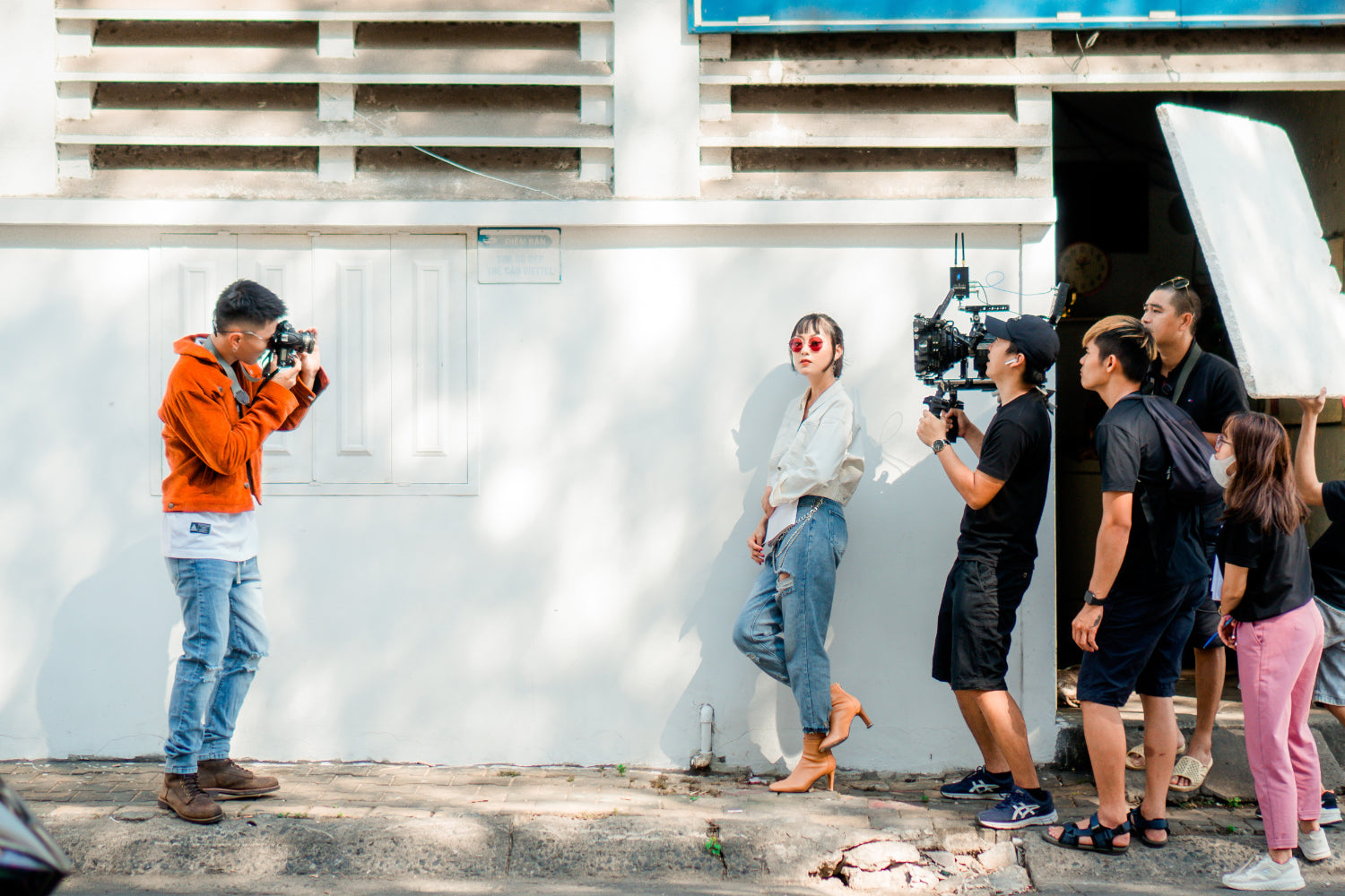 A videographer shoots a model posing while production staff assist from outside the frame