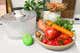 A plate full of fruits and vegetables, next to a vegetable brush and a salad spinner.