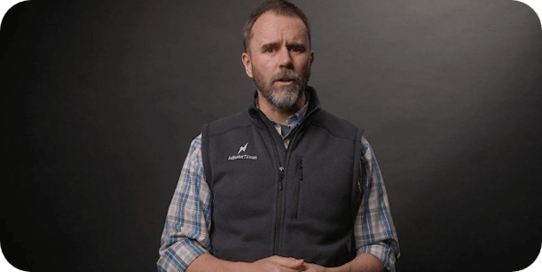 Man in professional attire with Adjuster TV Plus logo, conveying expertise in the insurance adjustment field, standing against a dark background for an educational video presentation