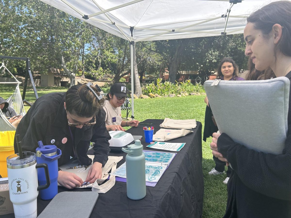 Wellness Coordinator and graduate student Cari Monraz irons on a patch while customizing graduate student Nadia Fahmi's tote bag.