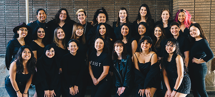 Photo of 24 people wearing all black and smiling at the camera.