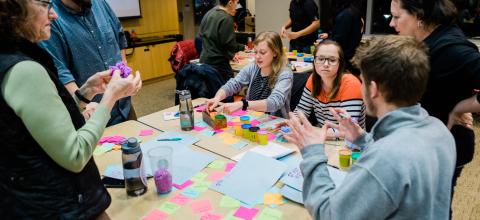 Students around a table with colorful papers and objects.