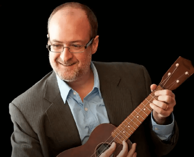 Picture of Christian smiling and playing a Ukulele.