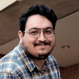 Kevin is facing forward and smiling. He has short brown hair and wears a green plaid shirt.