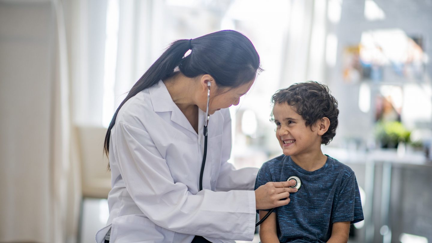 Boy smiling while the doctor checks his heart rate with a stethoscope.