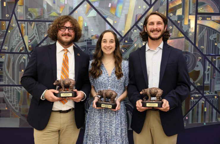 Two brothers and a sister, all Mercer students, stand together for a photo in front of a mirror mural while dressed up in nice attire.