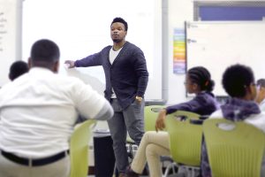 A person standing and pointing to something on a whiteboard in a classroom.