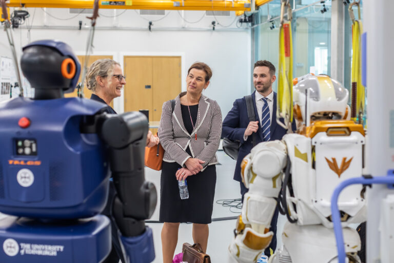 Three people viewing a display of two robots