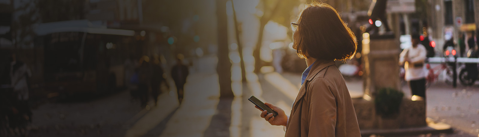 Woman holding her phone while walking in the city during golden hour