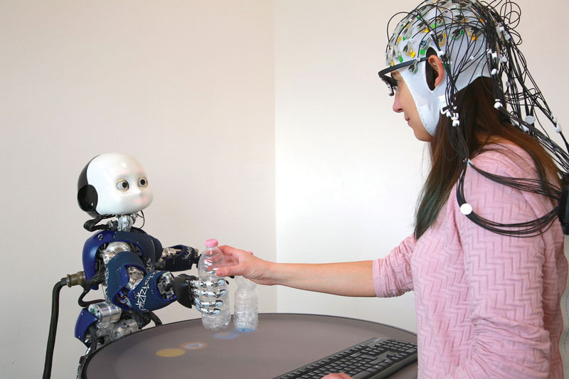 Figure 1. An example experimental setup where a participant is involved in an interaction with the humanoid robot iCub [3], while neuro-cognitive mechanisms are measured through performance data, as well as eye tracking and EEG.