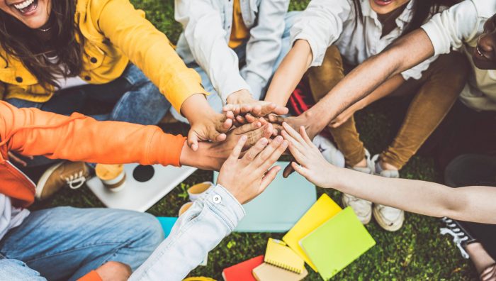 Multicultural university students stacking hands together in college campus - Young people hugging outside symbolizing unity and teamwork