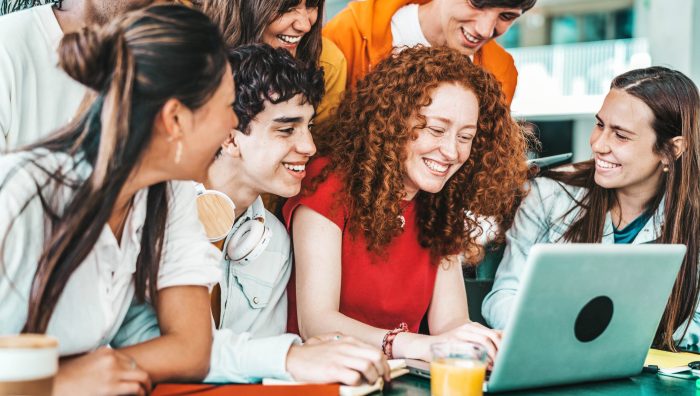 Multiracial university students sitting together at table with books and laptop - Happy young people doing group study in high school library - Life style concept with guys and girls in college campus