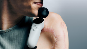 A person holding the Xbox Adaptive Joystick between their chin and collarbone