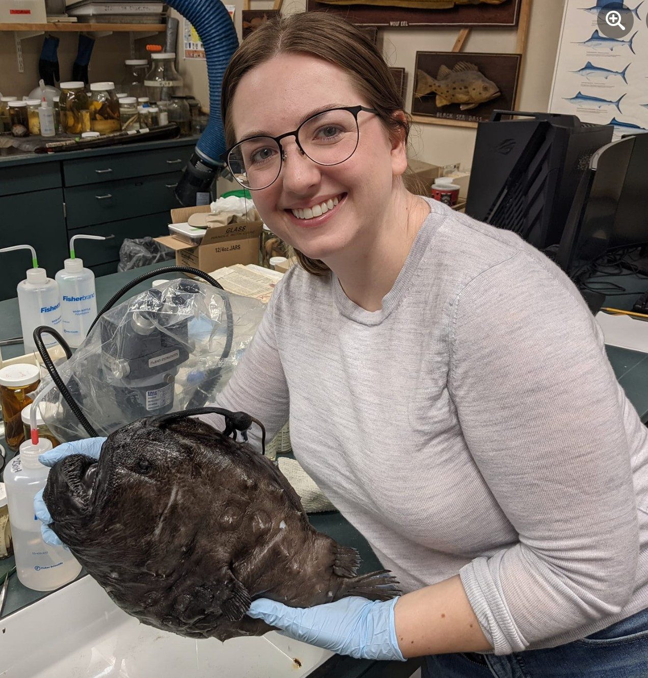 A woman smiles into the camera while holding a footballfish specimen