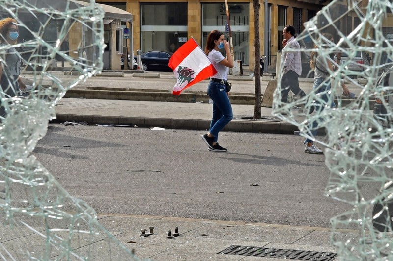 A woman walks with a Lebanese national flag tucked into her pocket past a broken window amid protests against dire economic conditions in Beirut.