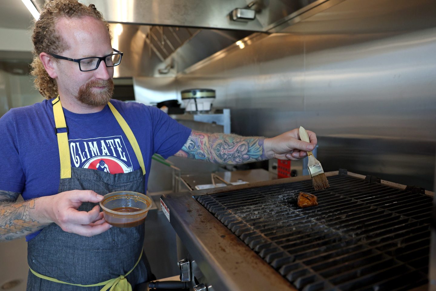 A man brushes a piece of lab-grown meat sitting on a grill