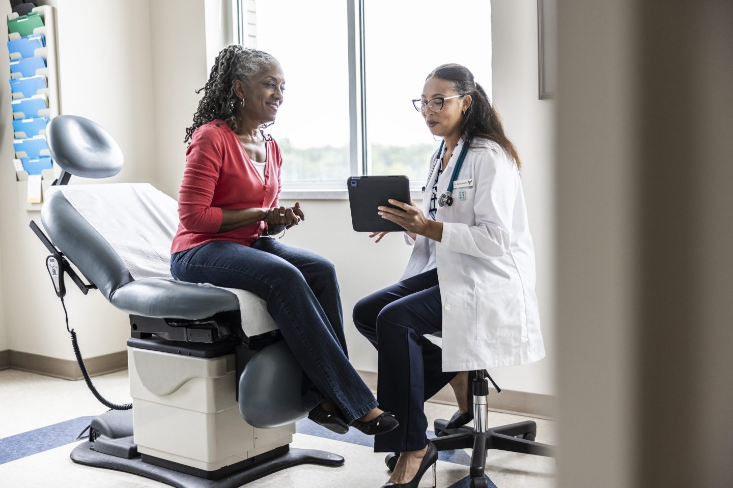 Female doctor and senior woman looking at digital tablet in exam room