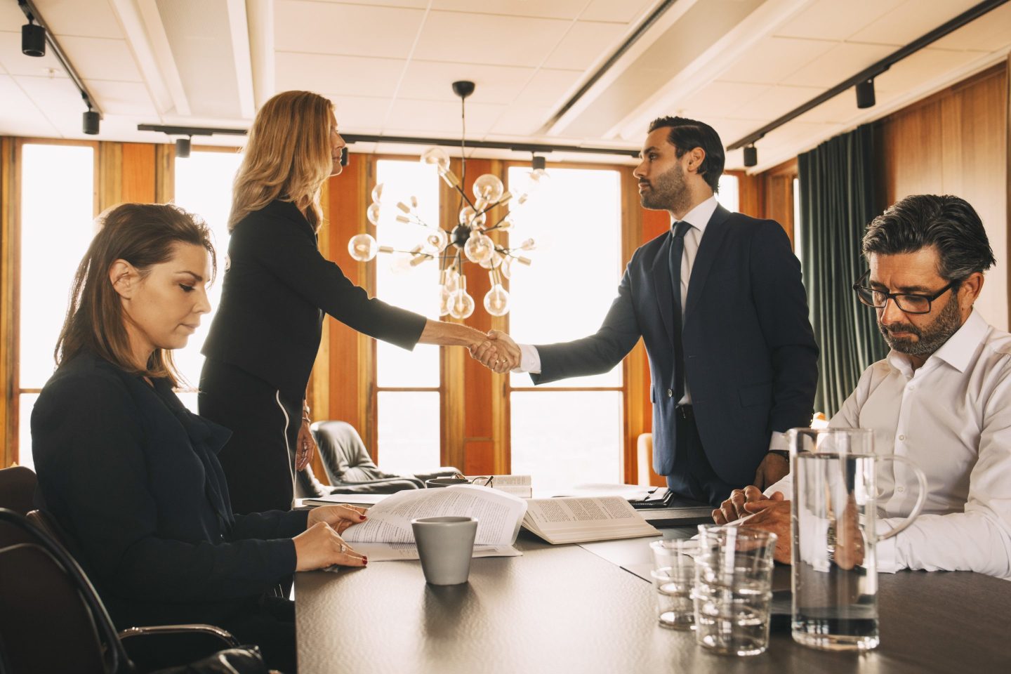 Male and female coworkers working while lawyers shaking hands at table in law office