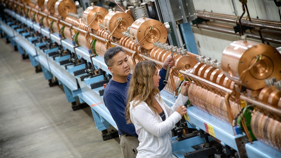 Two people stand near a linear accelerator