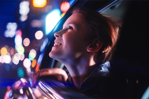 a child looking out the window of a car at a neon night