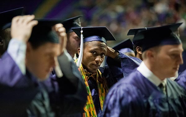 A young man of color at a Penn State graduation ceremony, moving the tassel on his cap