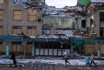 أشخاص يمرون أمام مبانٍ مدمرة في كوراخوف، أوكرانيا.