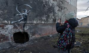 A teenager takes a photograph of a work by British street artist Banksy in the spring of 2023 in Irpin.