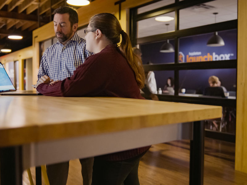 Two people standing beside a long wooden desk.