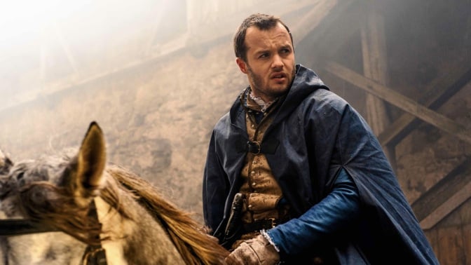 Matthew Shardlake from "Shardlake" rides a horse while wearing a blue cloak.