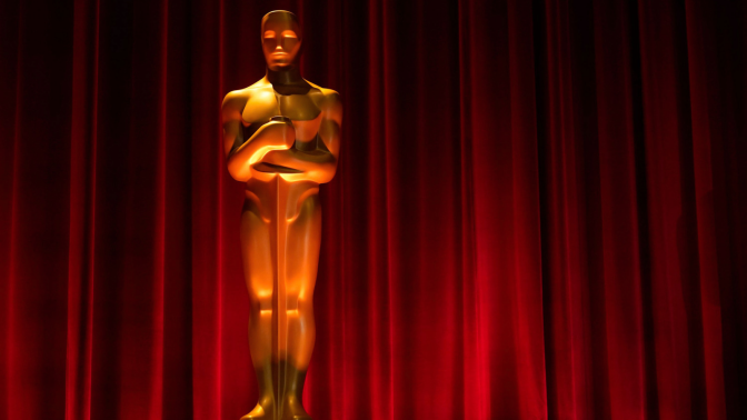 A golden statue is lit with a red curtain in the background. 