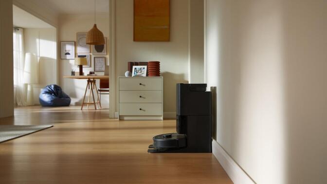 Black Roborock Qrevo S robot vacuum on self-empty dock sitting against wall with living room scene in background