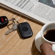 a tile tracker is attached to a keyring that sits on a tabletop next to a cup of coffee