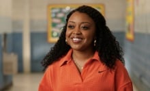 Janine Teagues from "Abbott Elementary" standing in a hallway in an orange blouse.