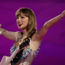 Taylor Swift smiling and raising her arms while performing at The Eras Tour.