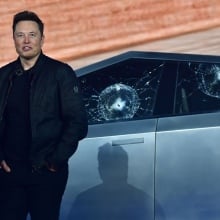 Elon Musk standing in front of a Cybertruck with two bullet marks in its windows.