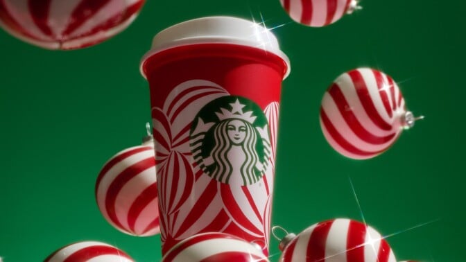 a starbucks reusable red cup covered in a design of white peppermint ornaments against a green background with ornaments surrounding it