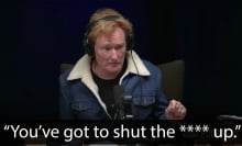 A man sits at a table in a dark podcast studio.