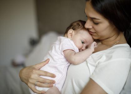 Young woman holds tired-looking baby as the baby touches her necklace