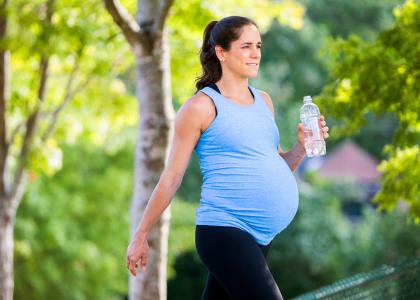 Pregnant woman walking outside carrying a bottle of water