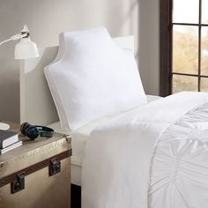 an unmade bed with white sheets and pillows on top of it next to a suitcase