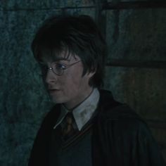 harry potter is standing in front of a stone wall and looking at the camera with an intense look on his face