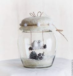 two white birds in a glass jar with pine cones and twine on the top