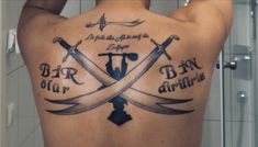 the back of a man's tattoo with two crossed swords and words on it