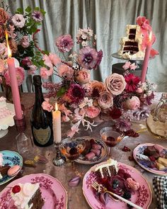 a table topped with pink plates covered in cake and desserts next to tall candles