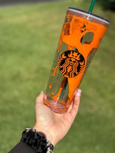 a person holding up a starbucks cup with orange straws on the outside and green grass in the background