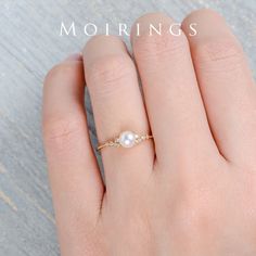 a woman's hand wearing a gold ring with a white pearl and diamond accent