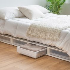 a bed with two drawers underneath it and a plant in the corner next to it