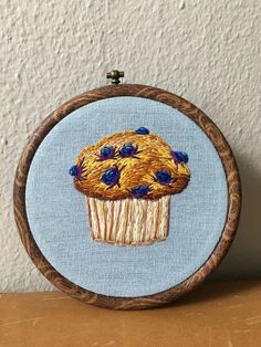 an embroidered picture of a cupcake with blueberries on it, sitting on a table